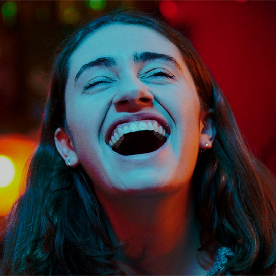 Close up of a person laughing with eyes closed - their face is bathed in blue light 